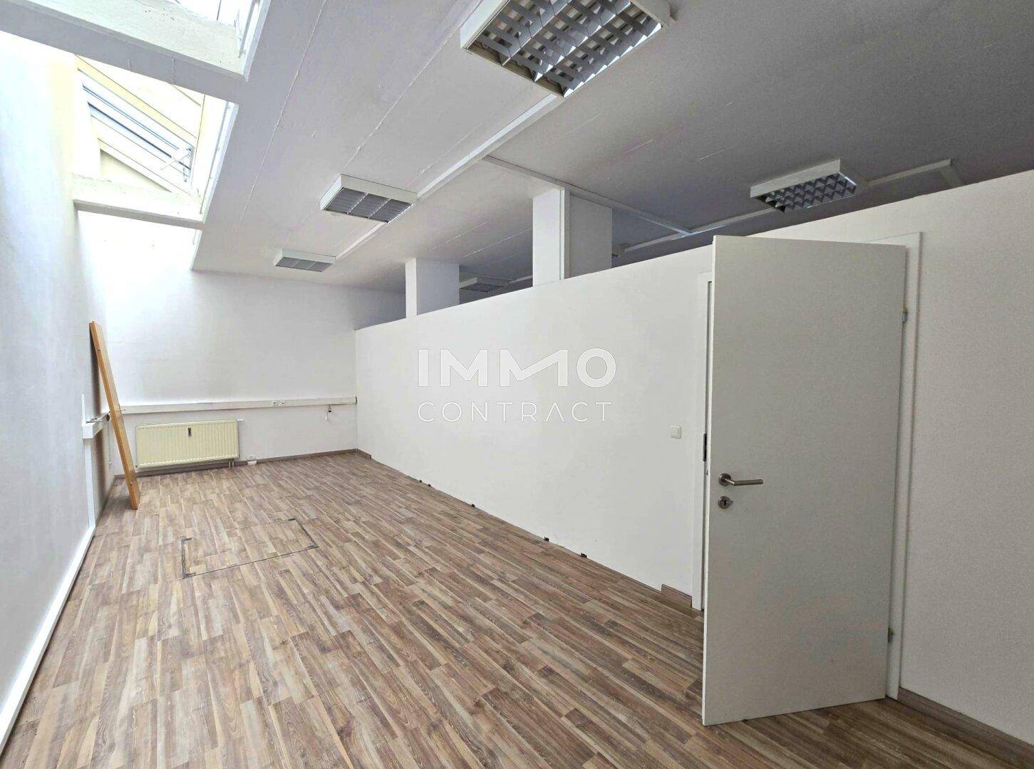 Bürobereich mit Trennwand, Holzboden und einem Oberlicht, das zusätzliches Tageslicht spendet.