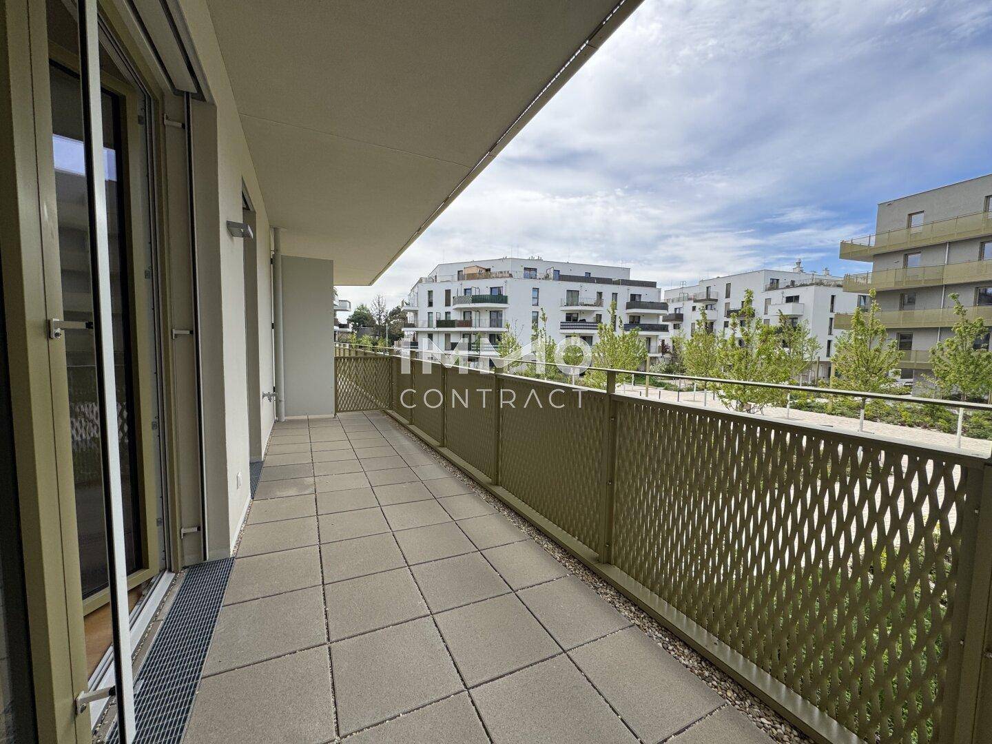 Langer Balkon mit Fliesenboden und Blick auf die moderne Wohnanlage.
