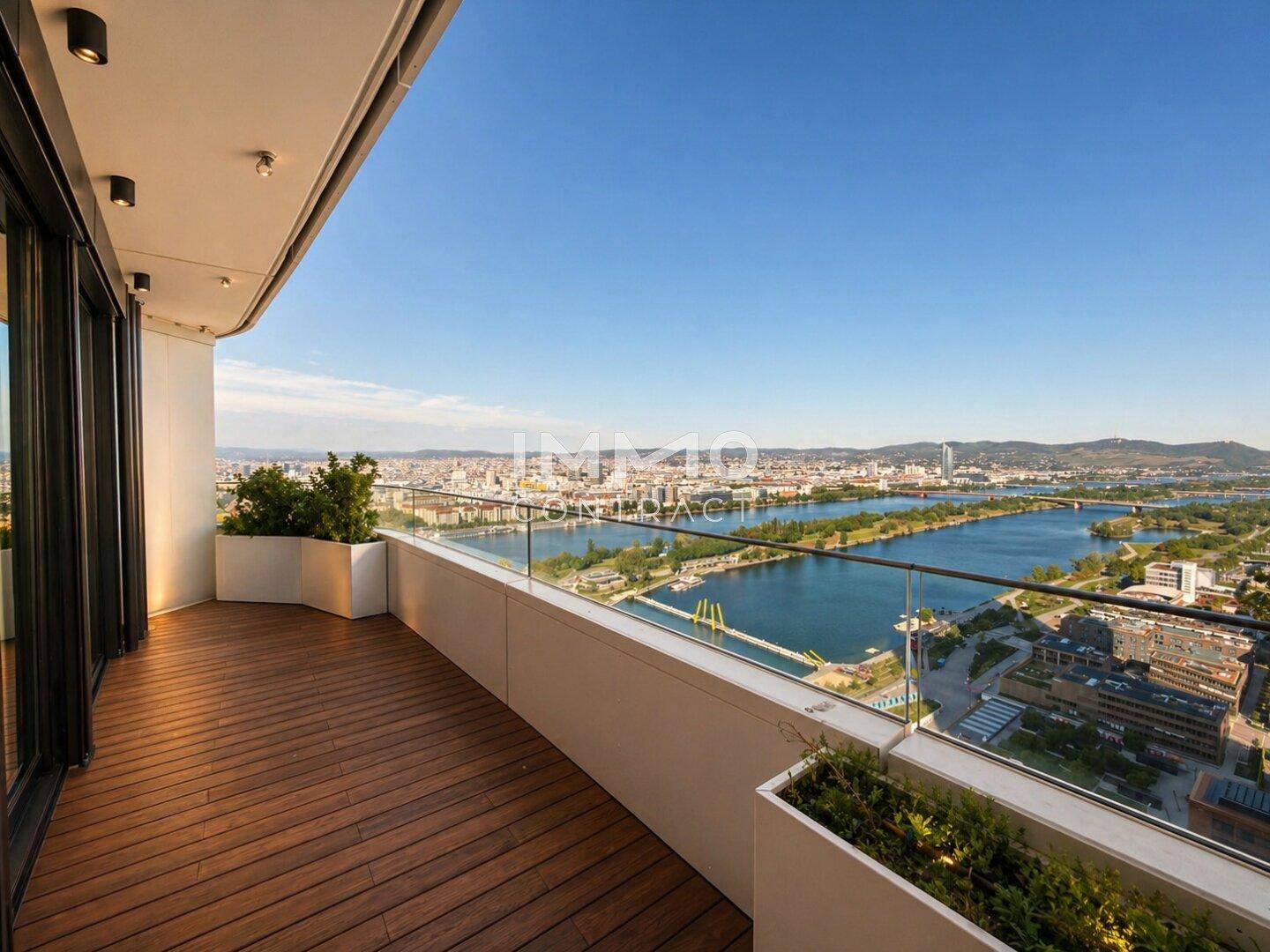 Geräumiger Balkon mit Holzboden, Glasgeländer und weitem Blick über die Stadt und den Fluss.