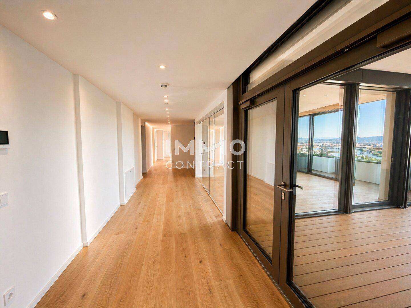 Langer, heller Flur mit Holzboden und Zugang zu einem Balkon mit Stadtblick.