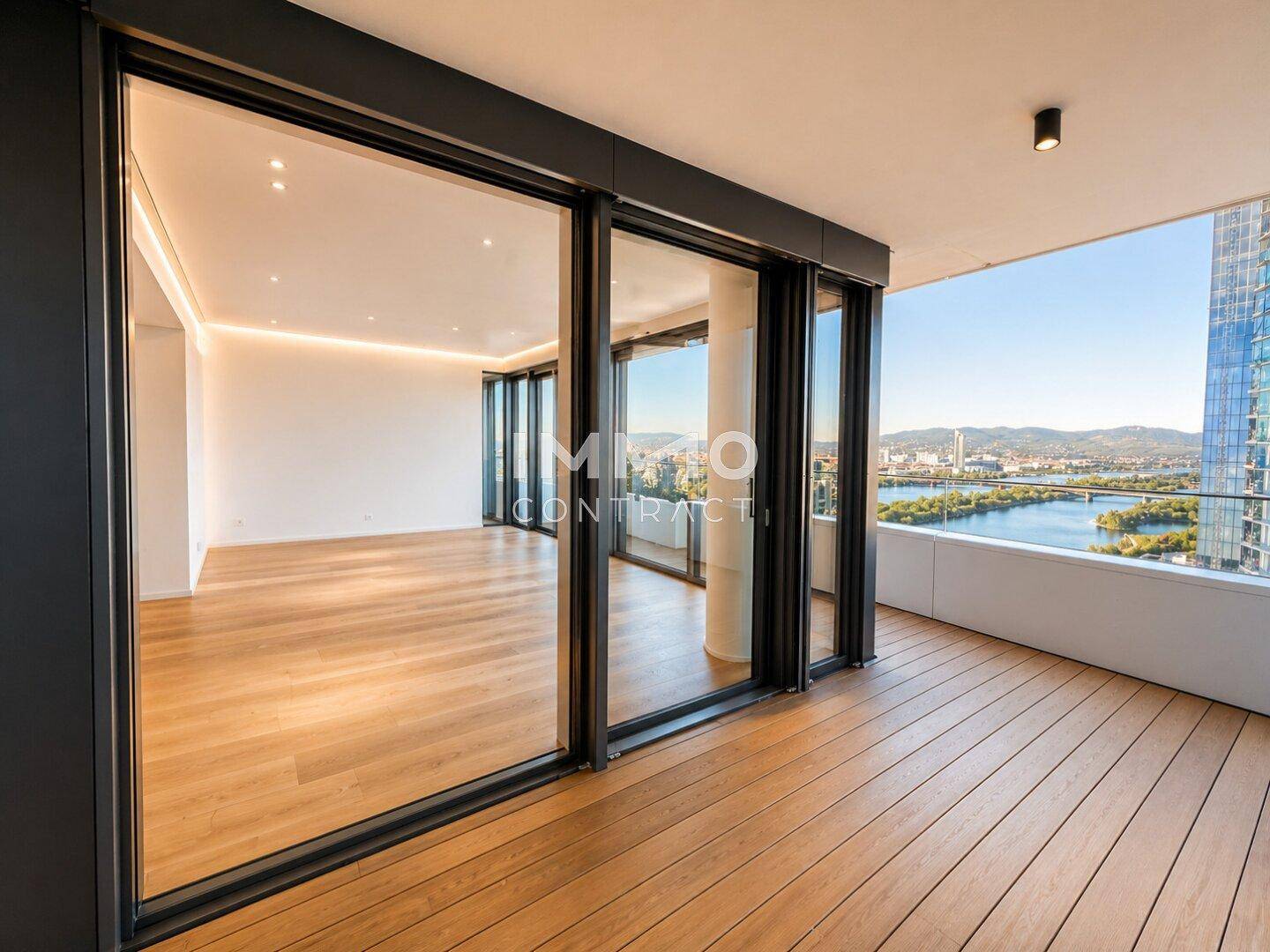 Moderner Balkon mit Holzboden und raumhohen Fenstern, die einen weiten Blick auf die Stadt bieten.