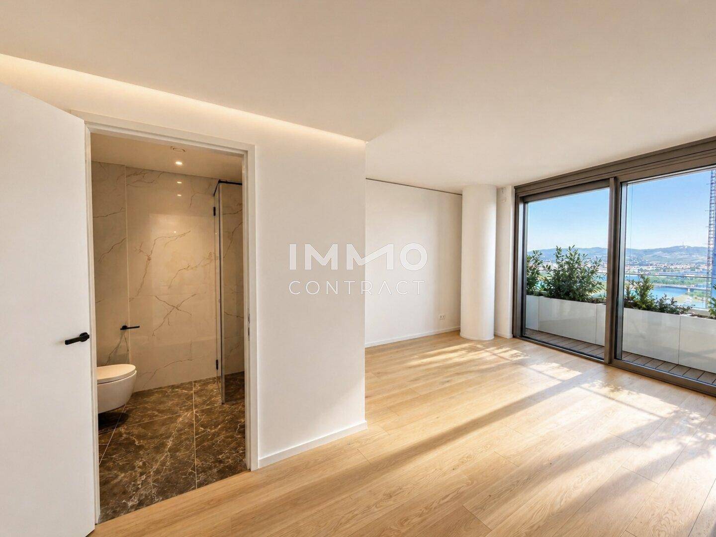 Schlafzimmer mit Holzboden, großen Fenstern und Zugang zu einem modernen Badezimmer.