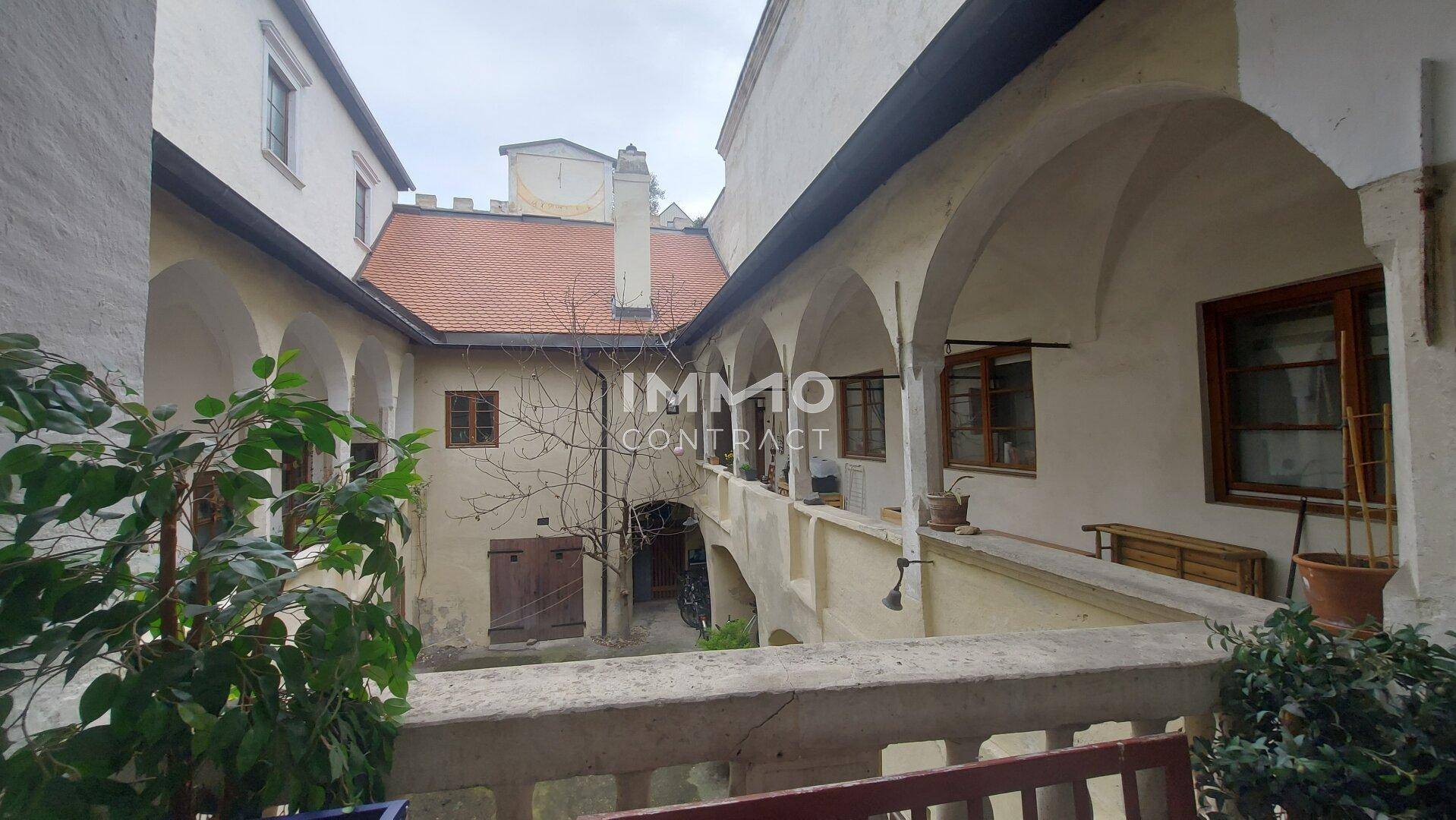 Blick von einer Loggia in den historischen Innenhof mit Arkaden und alten Dächern.