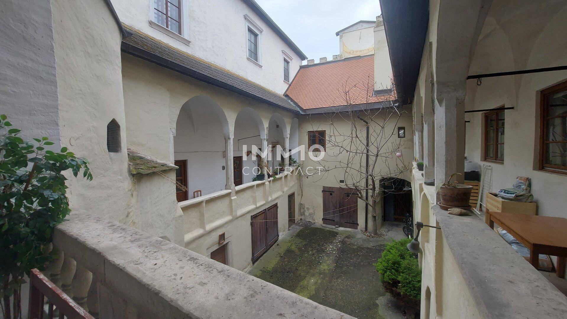 Weitläufiger Blick von einer Loggia in den historischen Innenhof mit Arkaden und alten Dächern.