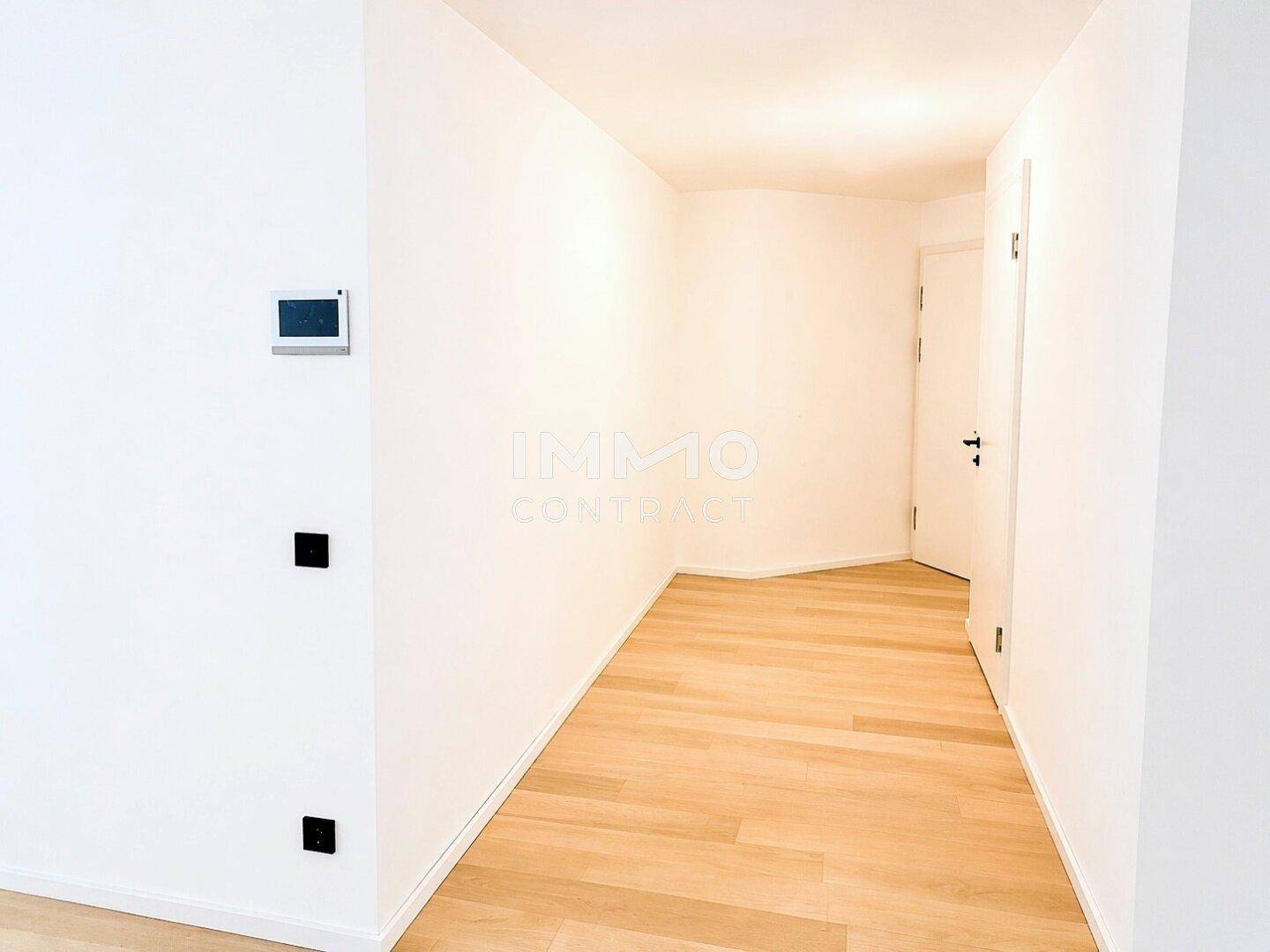 Heller Flur mit Holzparkett und weißen Wänden, führt zu weiteren Räumen der Wohnung.