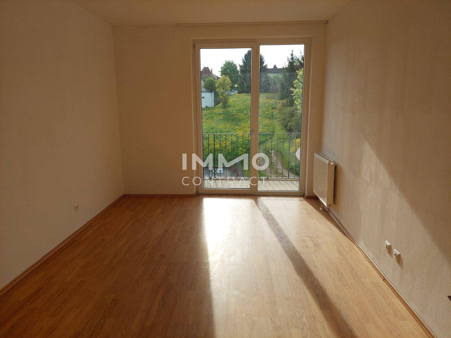 Helles Schlafzimmer mit Laminatboden und großem Fenster mit Blick ins Grüne.