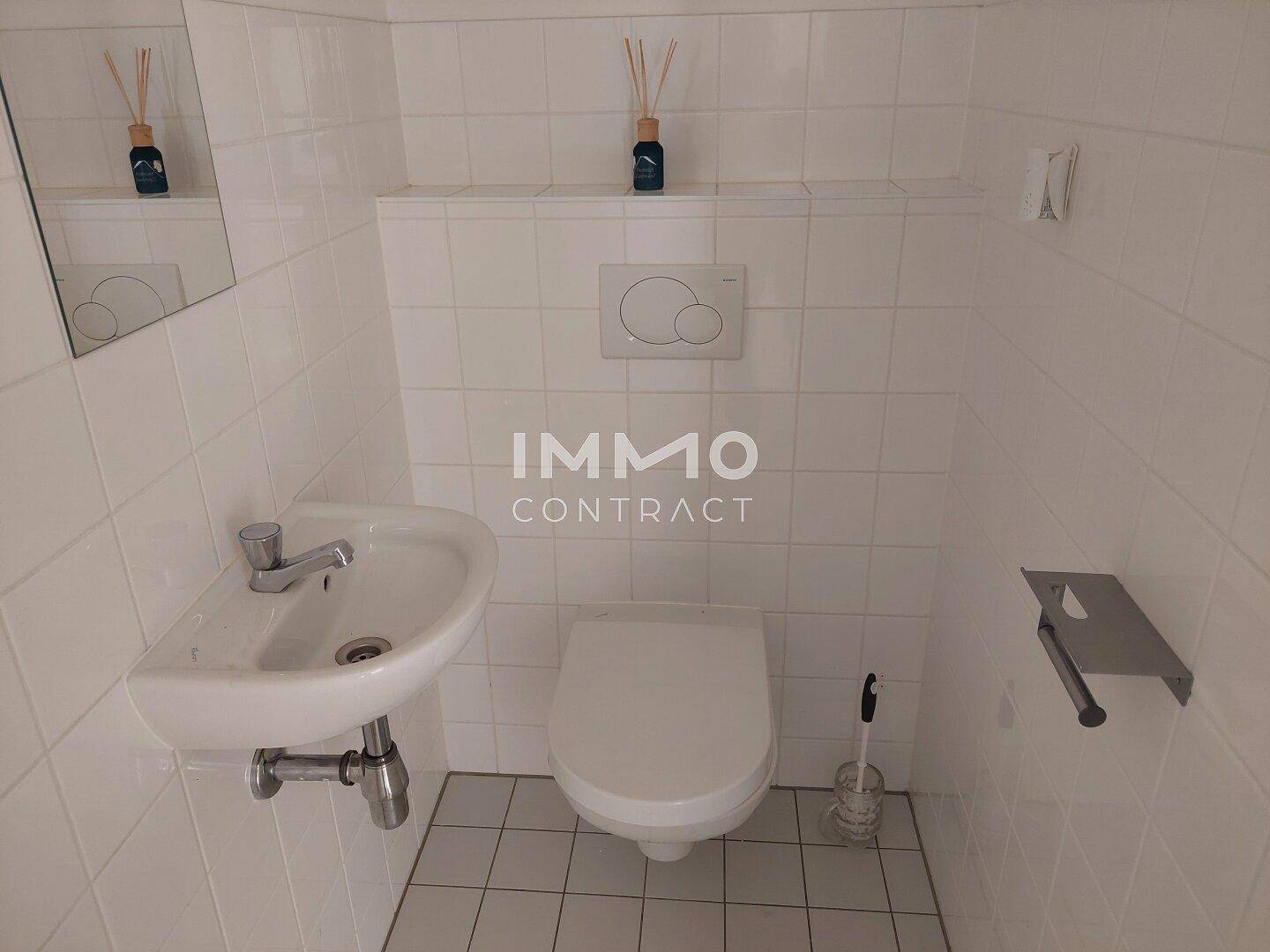 Kleines, vollständig gefliestes WC mit wandhängender Toilette und Handwaschbecken.