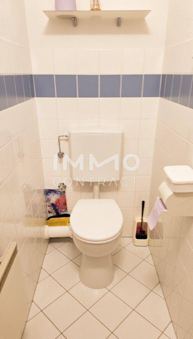 Kleines separates WC mit weißen Fliesen und blauen Akzentstreifen.