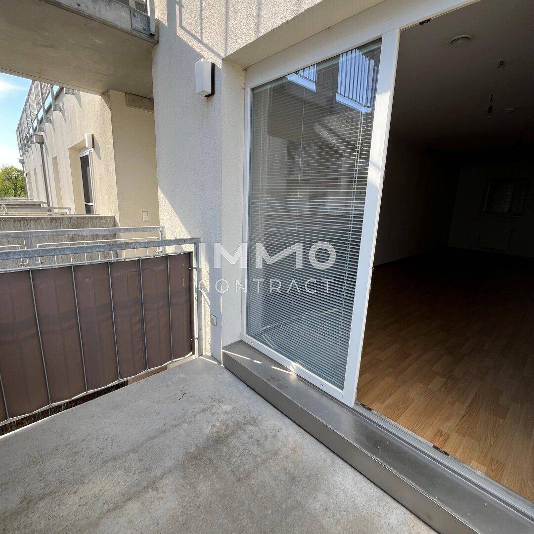 Betonbalkon mit Blick in den Wohnbereich durch eine große Schiebetür, bietet viel Tageslicht.