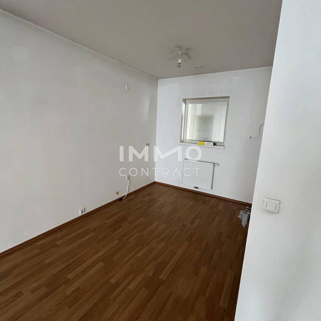 Leeres Schlafzimmer mit Laminatboden, weiß gestrichenen Wänden und einem Fenster für natürliches Licht.