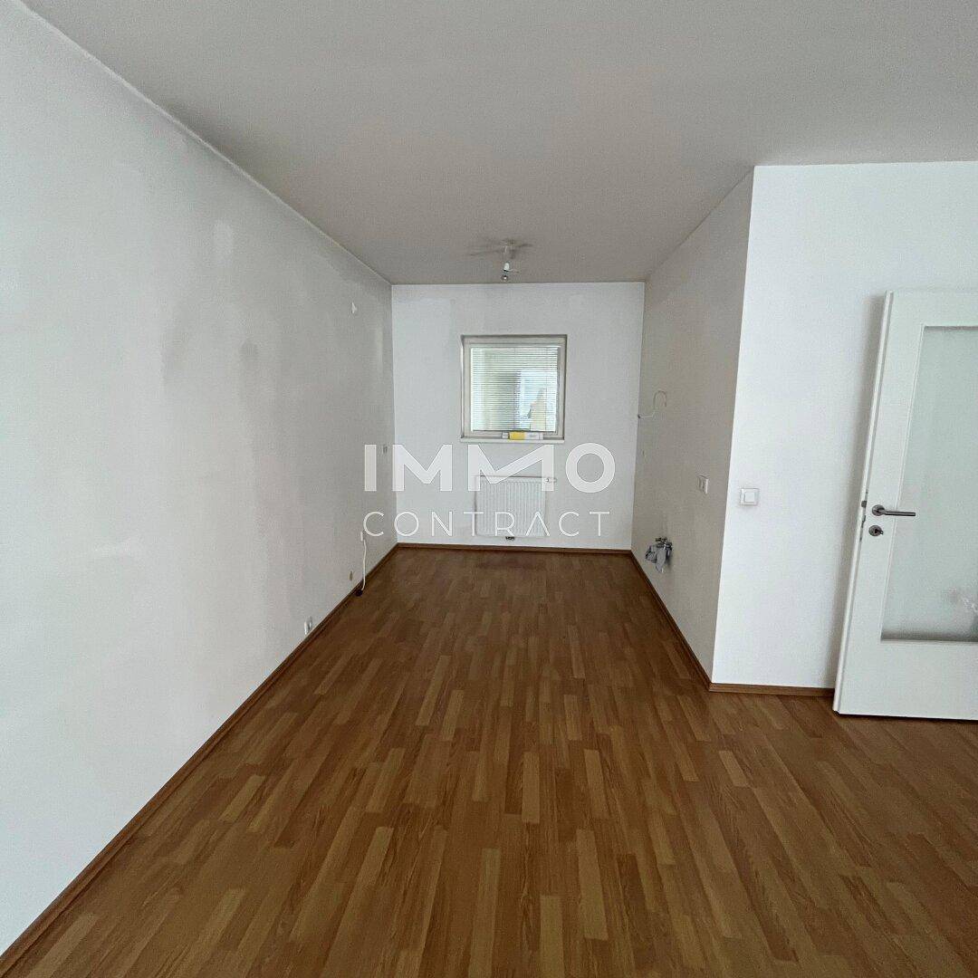 Helles, leeres Zimmer mit Laminatboden und weiß gestrichenen Wänden, bereit zur Einrichtung.