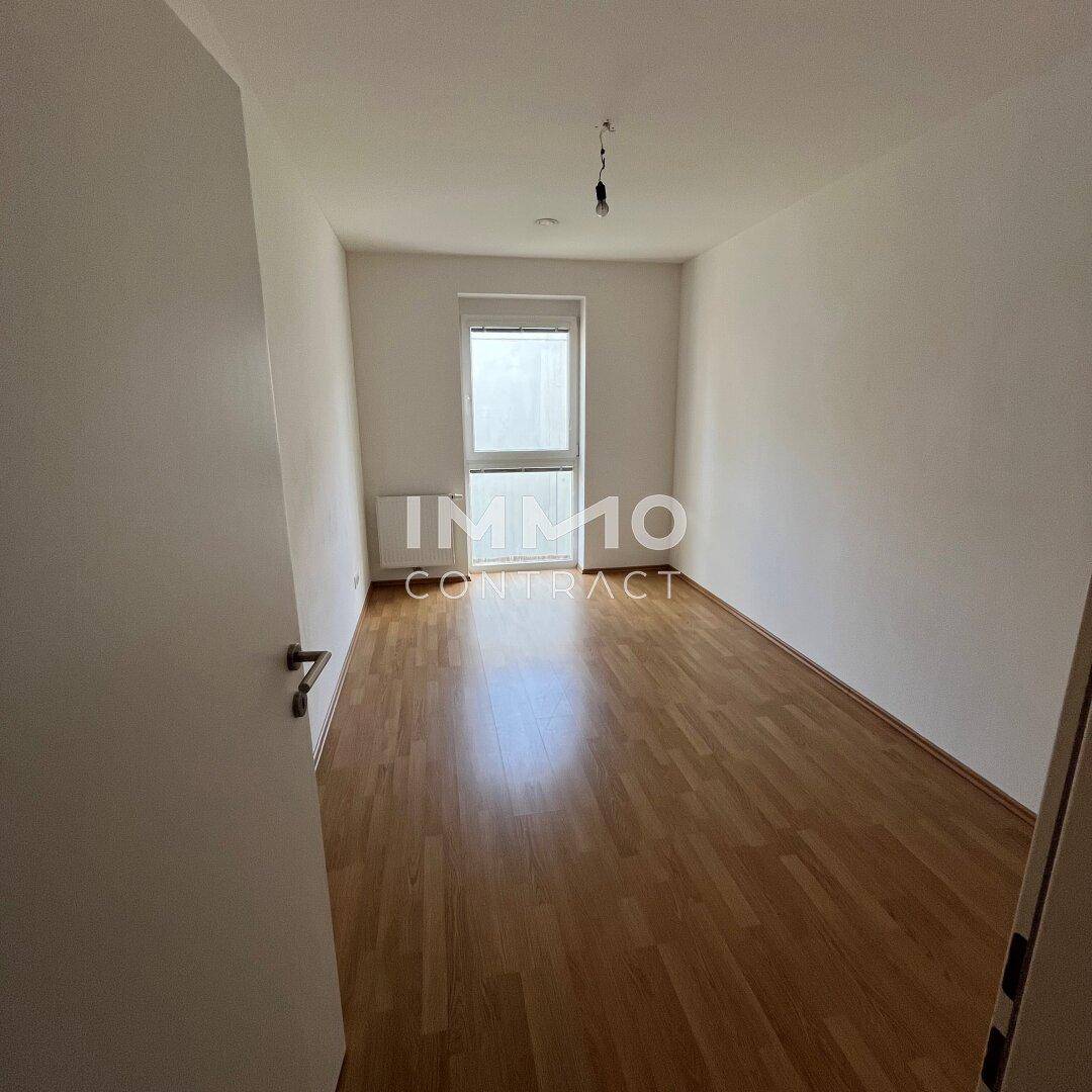 Leeres Schlafzimmer mit Laminatboden und Fenster, das viel Tageslicht hereinlässt.