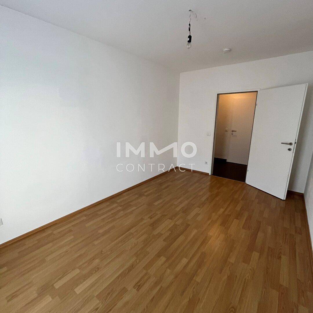 Leeres Zimmer mit Laminatboden und weißer Tür, bietet vielseitige Nutzungsmöglichkeiten.