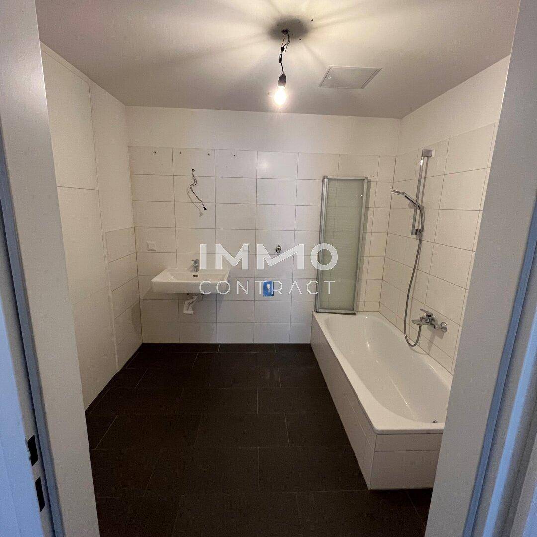 Badezimmer mit Badewanne, Waschbecken und dunklen Bodenfliesen, bereit zur Modernisierung.