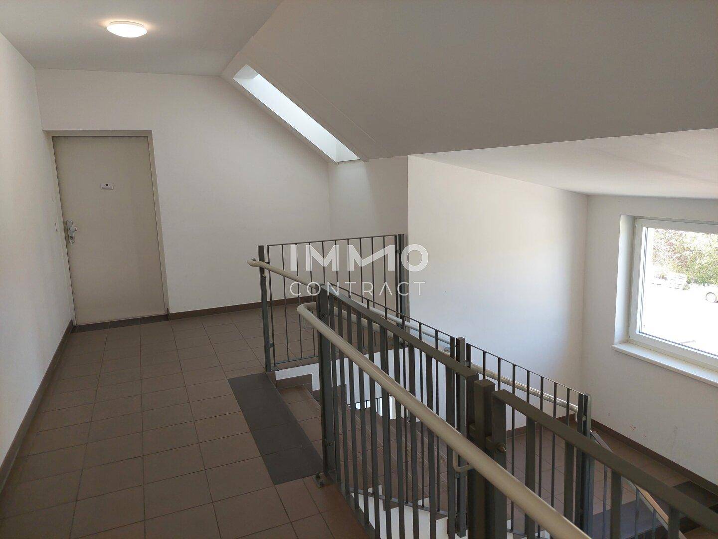 Treppenhaus mit Fliesenboden, Metallgeländer und Fenster für natürliche Belichtung zwischen den Etagen.