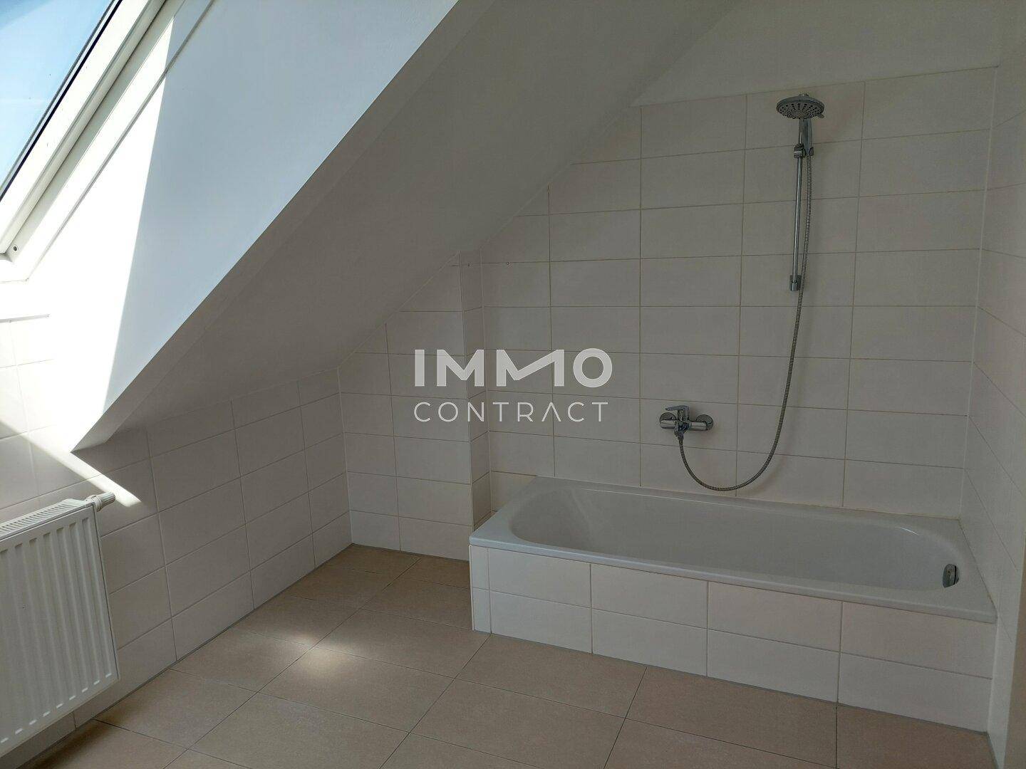 Helles Badezimmer mit Badewanne, weißen Fliesen und Dachfenster für natürliche Belüftung und Licht.