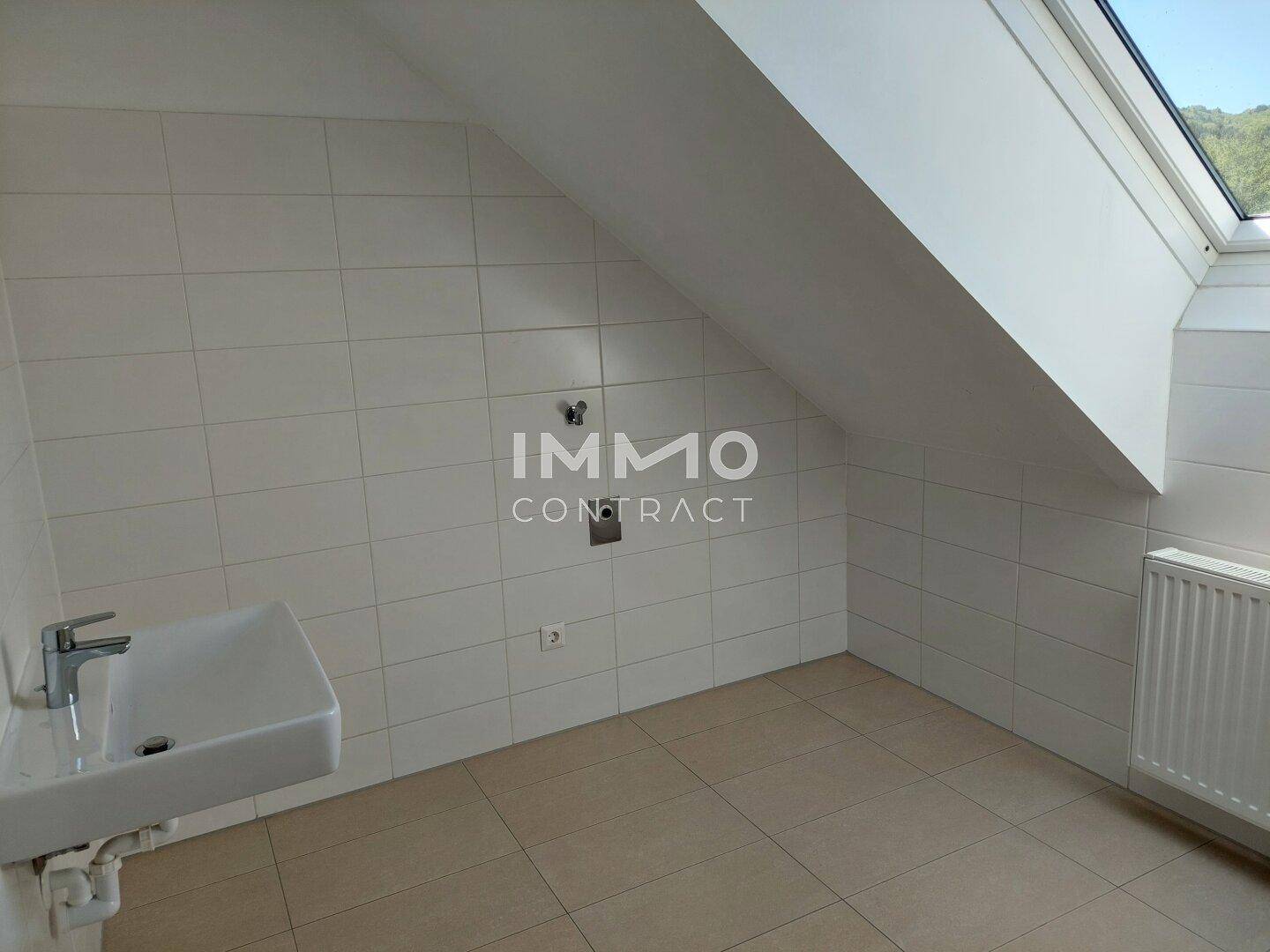 Helles Badezimmer mit Waschbecken, weißen Fliesen und Dachfenster unter der Dachschräge.