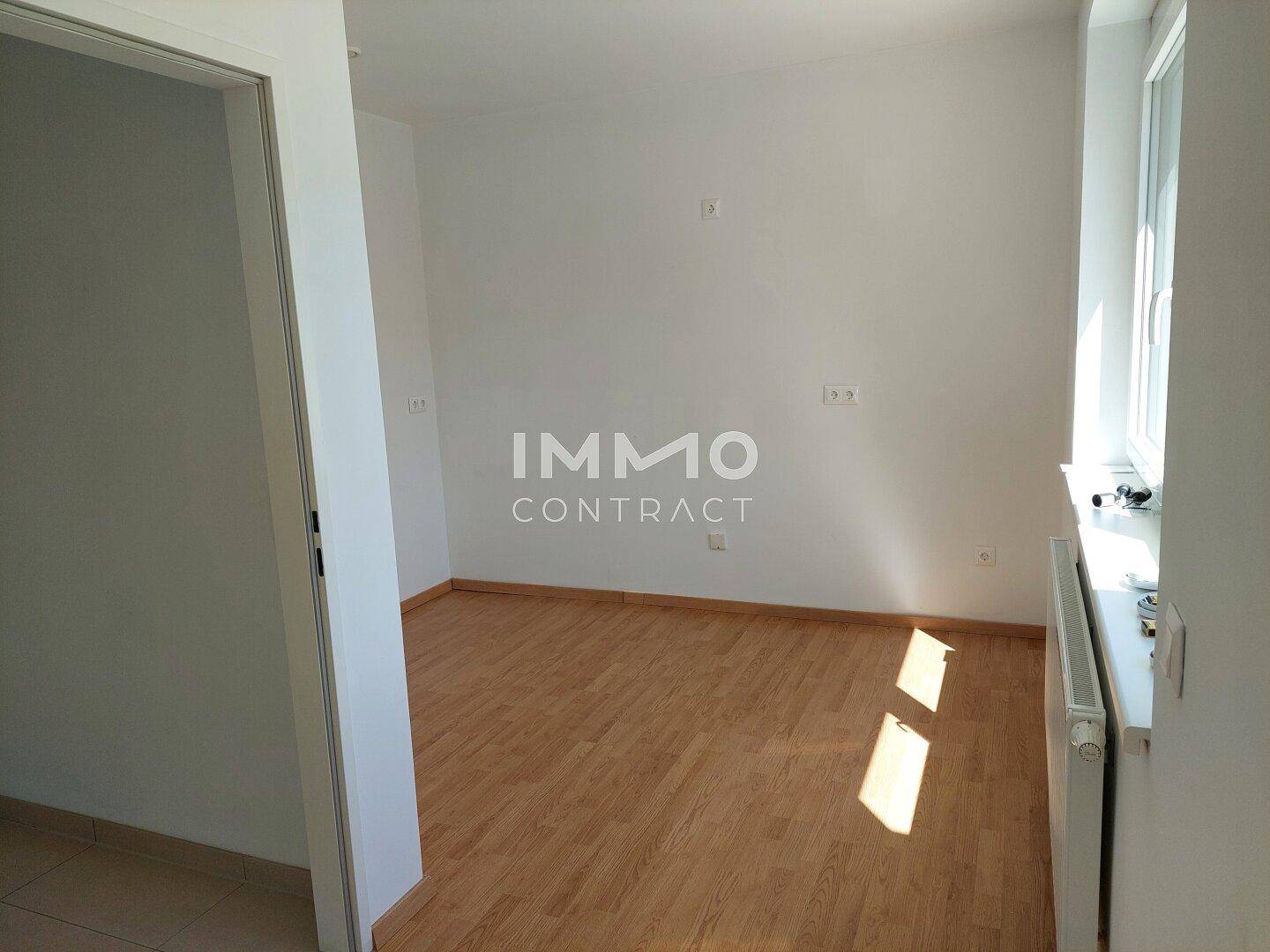Heller, leerer Raum mit Holzboden, Fenster und Heizkörper, bereit zur individuellen Einrichtung.