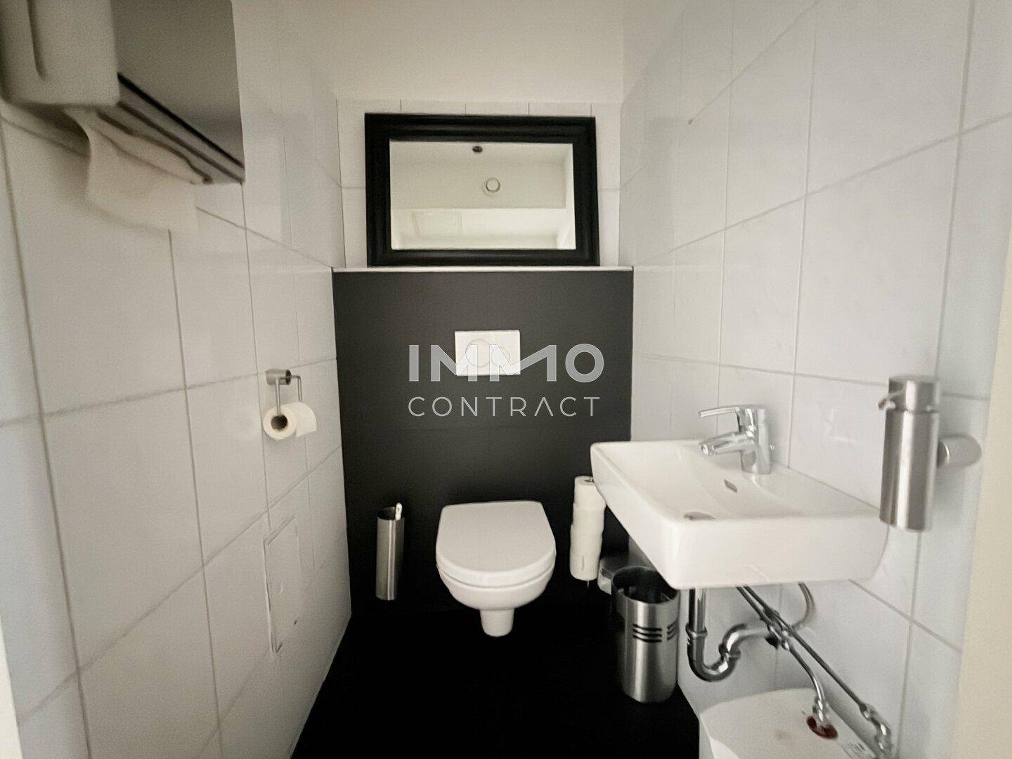 Modernes WC mit weißen Fliesen, schwarzer Akzentwand und kleinem Waschbecken, gut gepflegt.