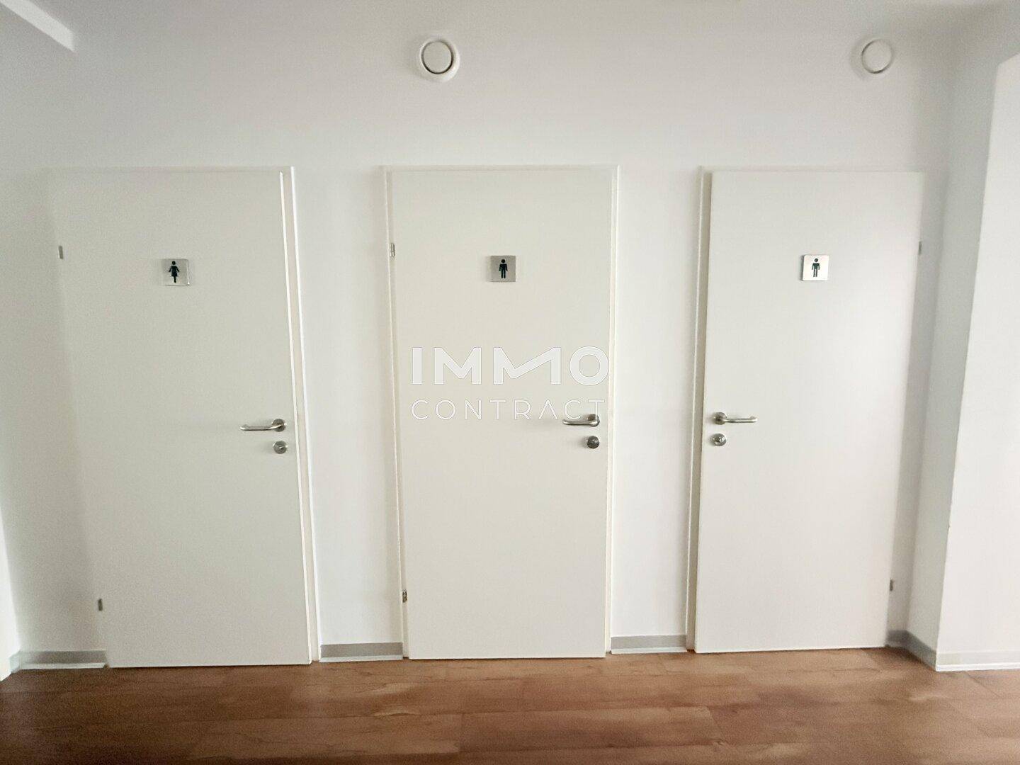 Flur mit drei weißen Türen, die zu den Toilettenräumen führen, mit Holzboden.