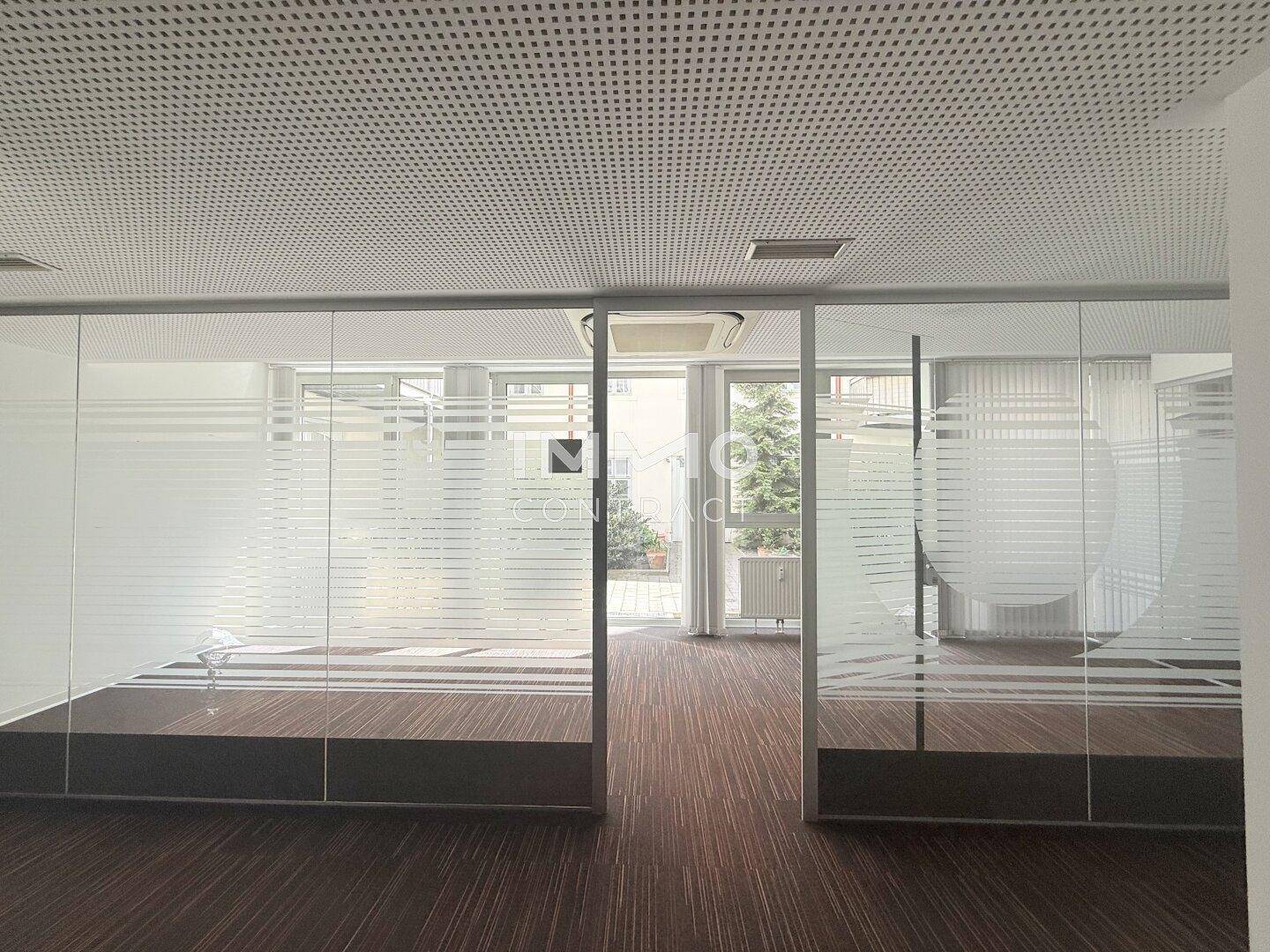 Großes Büro mit Teppichboden und Glaswänden, die den Raum unterteilen, mit viel Tageslicht.