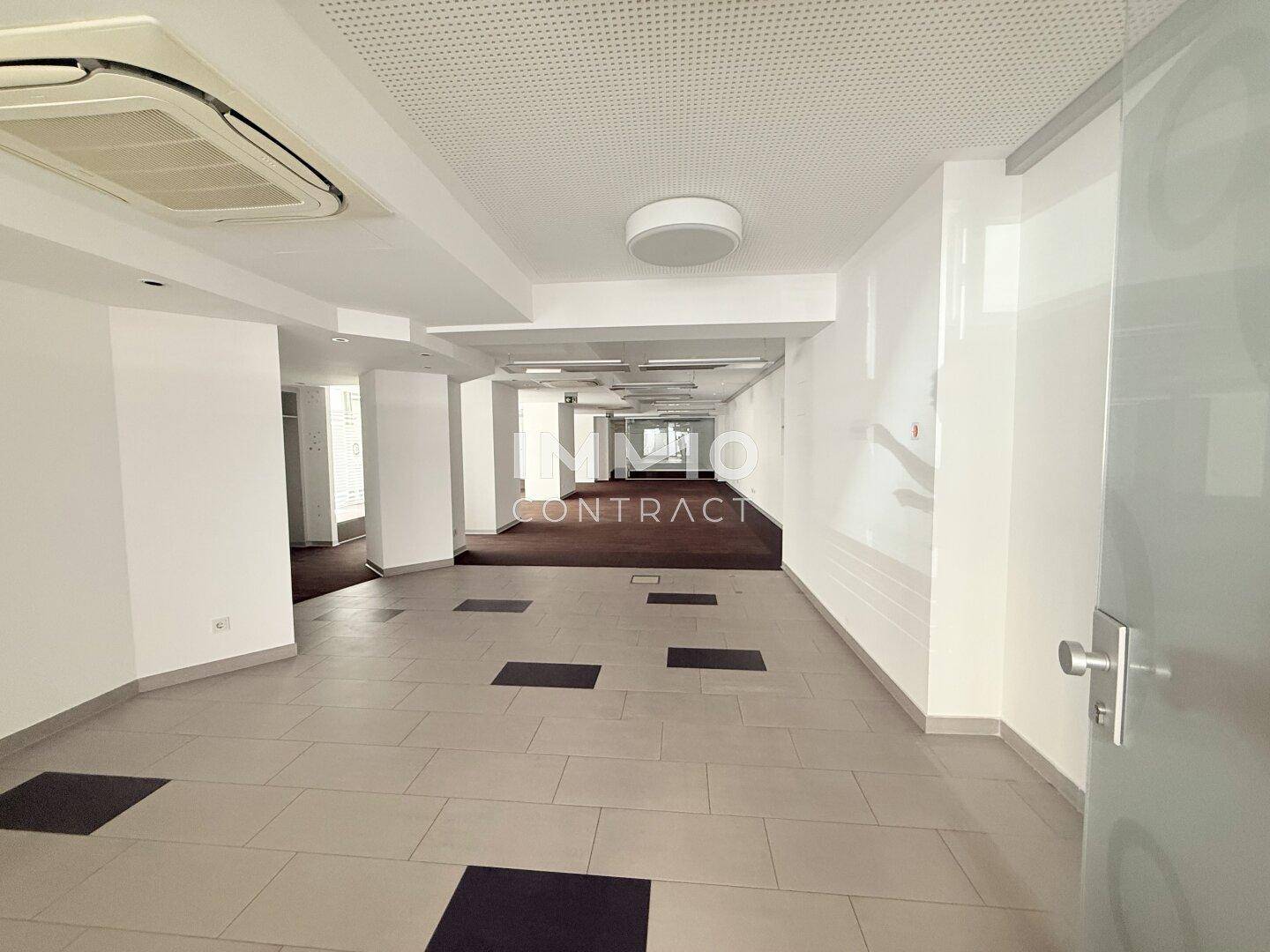 Langer Flur in einem Bürogebäude mit Fliesenboden und Blick auf weitere Büroräume, mit Klimaanlage.