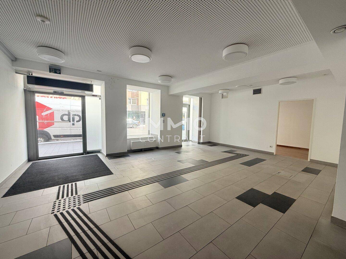 Heller Geschäftsraum mit großflächigen Fliesen und Zugang zur Straße durch eine Glastür, sauber und funktional.