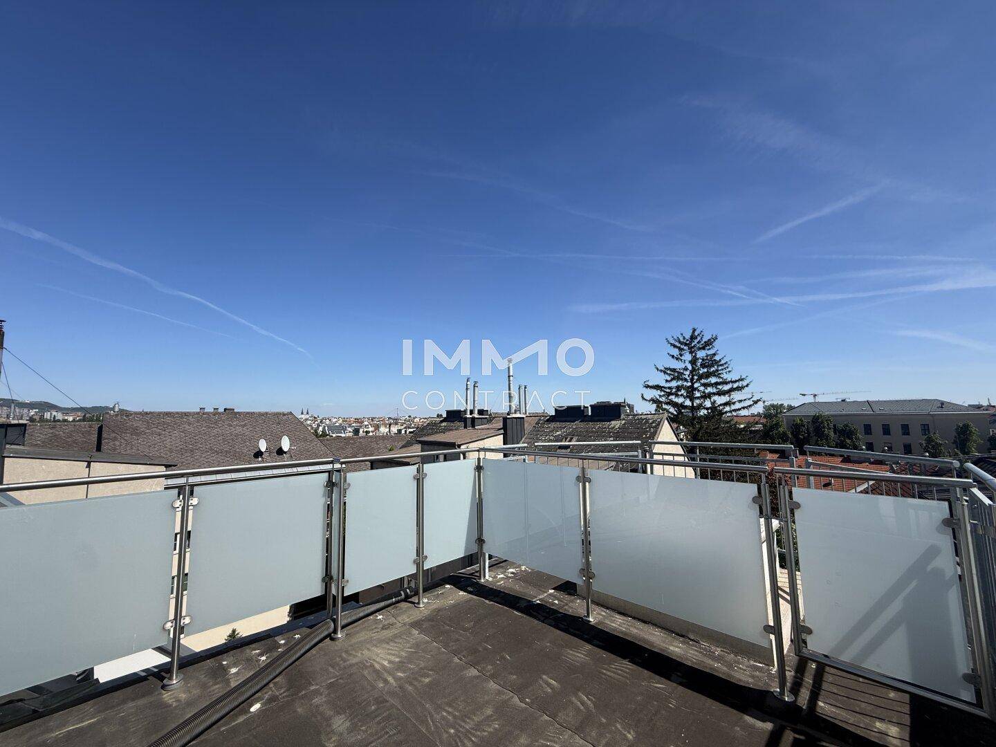 Geräumige Dachterrasse mit moderner Glasbrüstung und weitem Blick über die Dächer der Stadt.