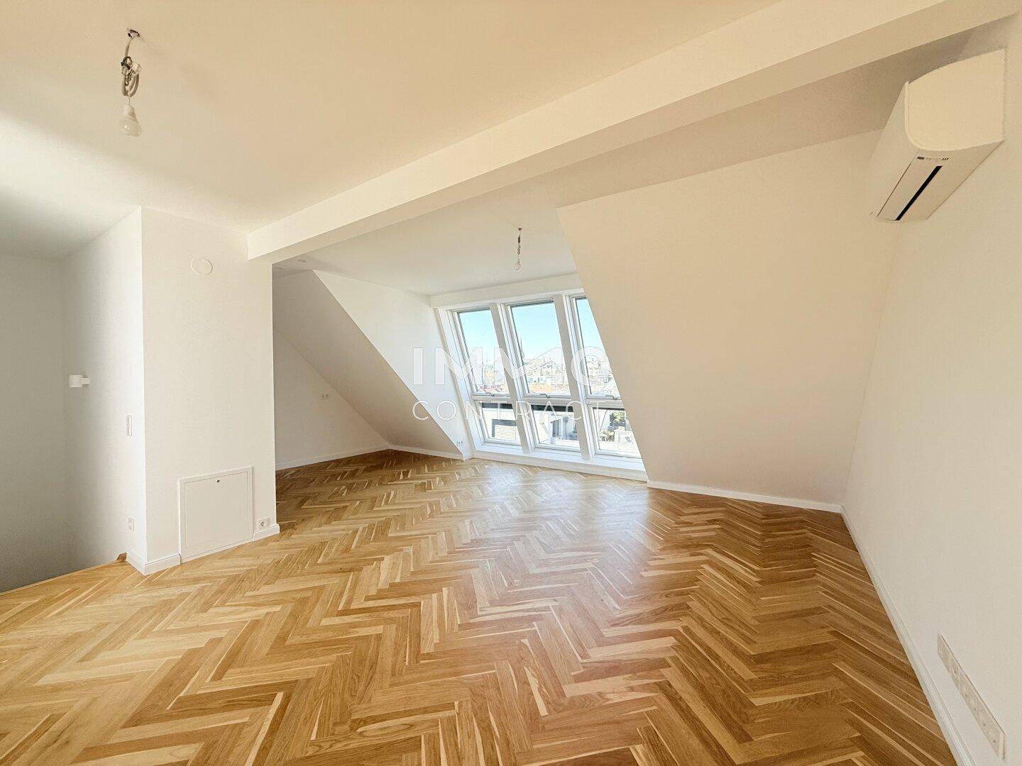 Geräumiges Dachgeschosszimmer mit Fischgrätparkett, Klimaanlage und schrägen Wänden.