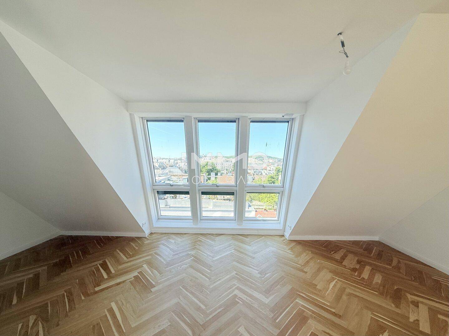 Lichtdurchflutetes Dachgeschosszimmer mit Fischgrätparkett und Panoramablick über die Stadt.