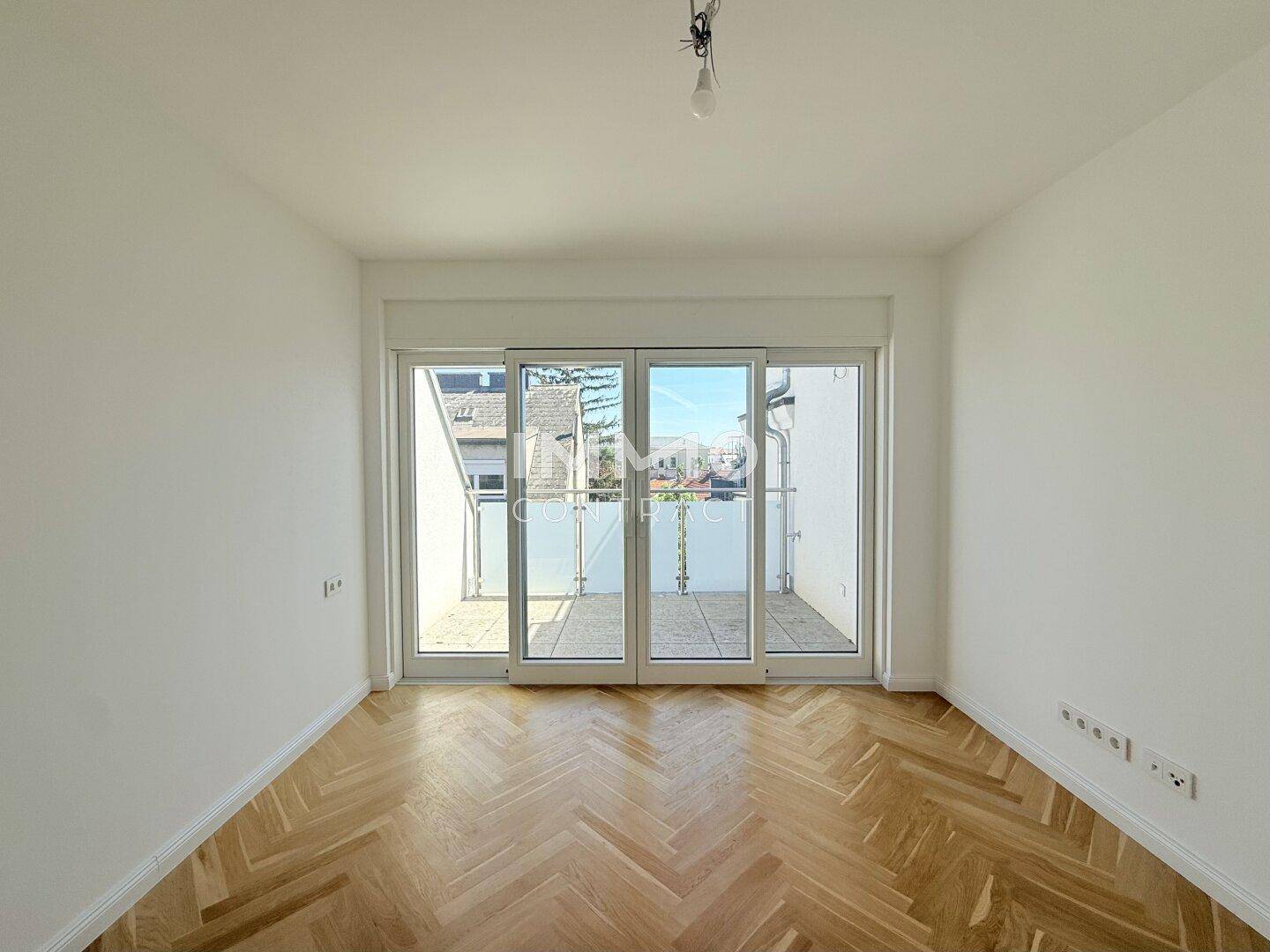 Heller Raum mit Fischgrätparkett und Zugang zu einer Terrasse durch große Glastüren.