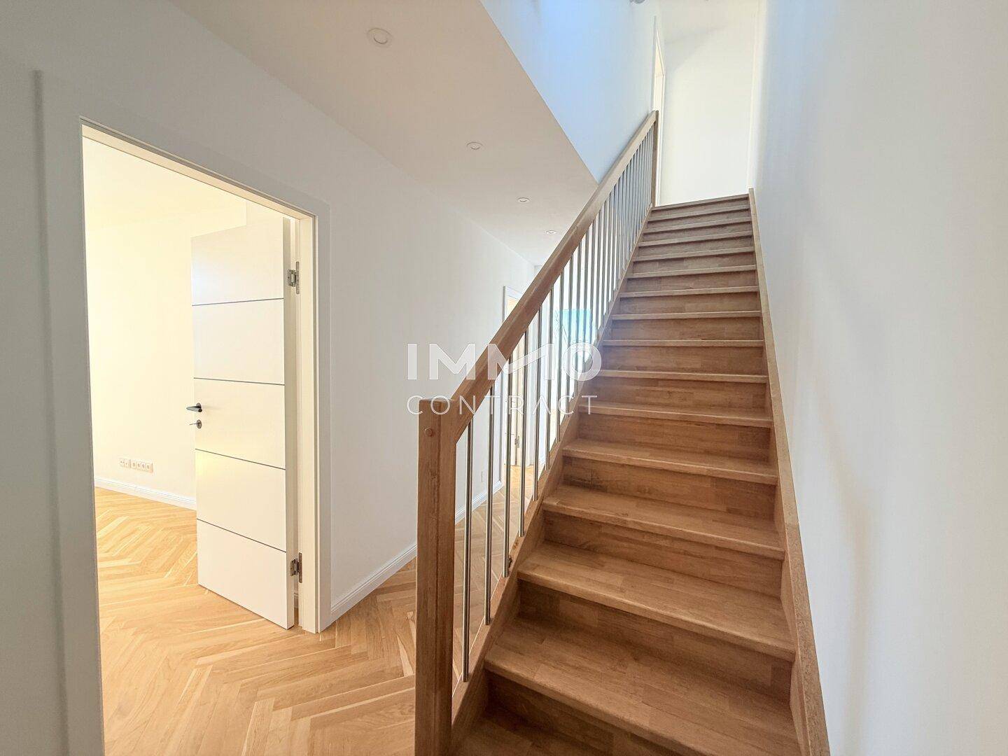 Heller Flur mit Holztreppe und Fischgrätparkett, der zu weiteren Räumen führt.
