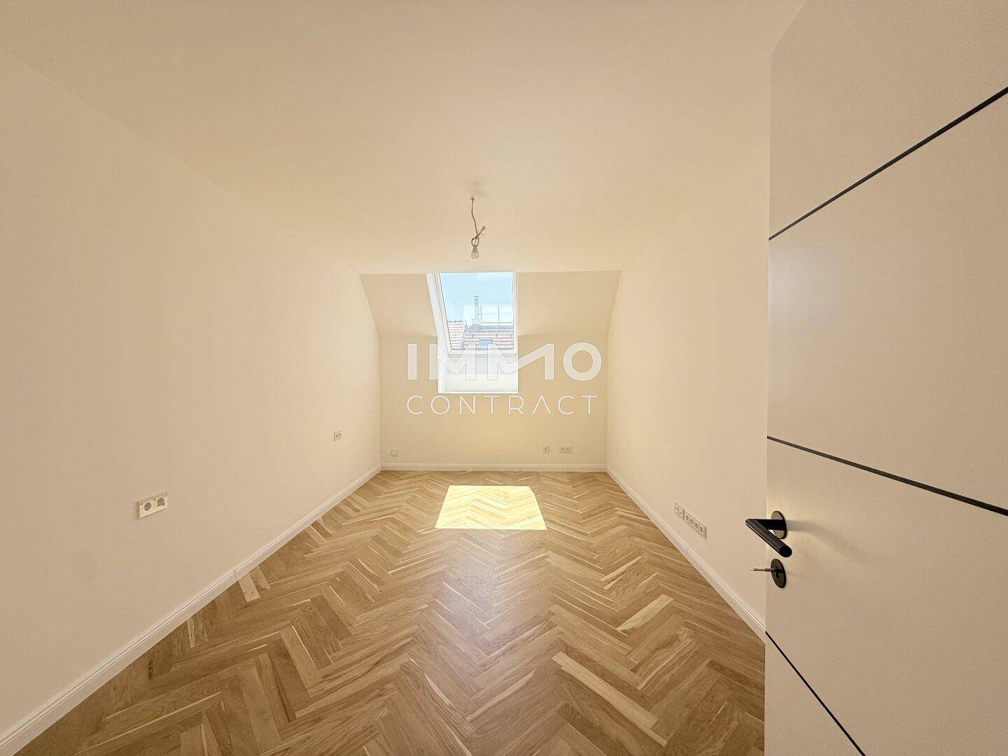 Geräumiges Schlafzimmer mit Fischgrätparkett, Dachschräge und einem großen Dachfenster.