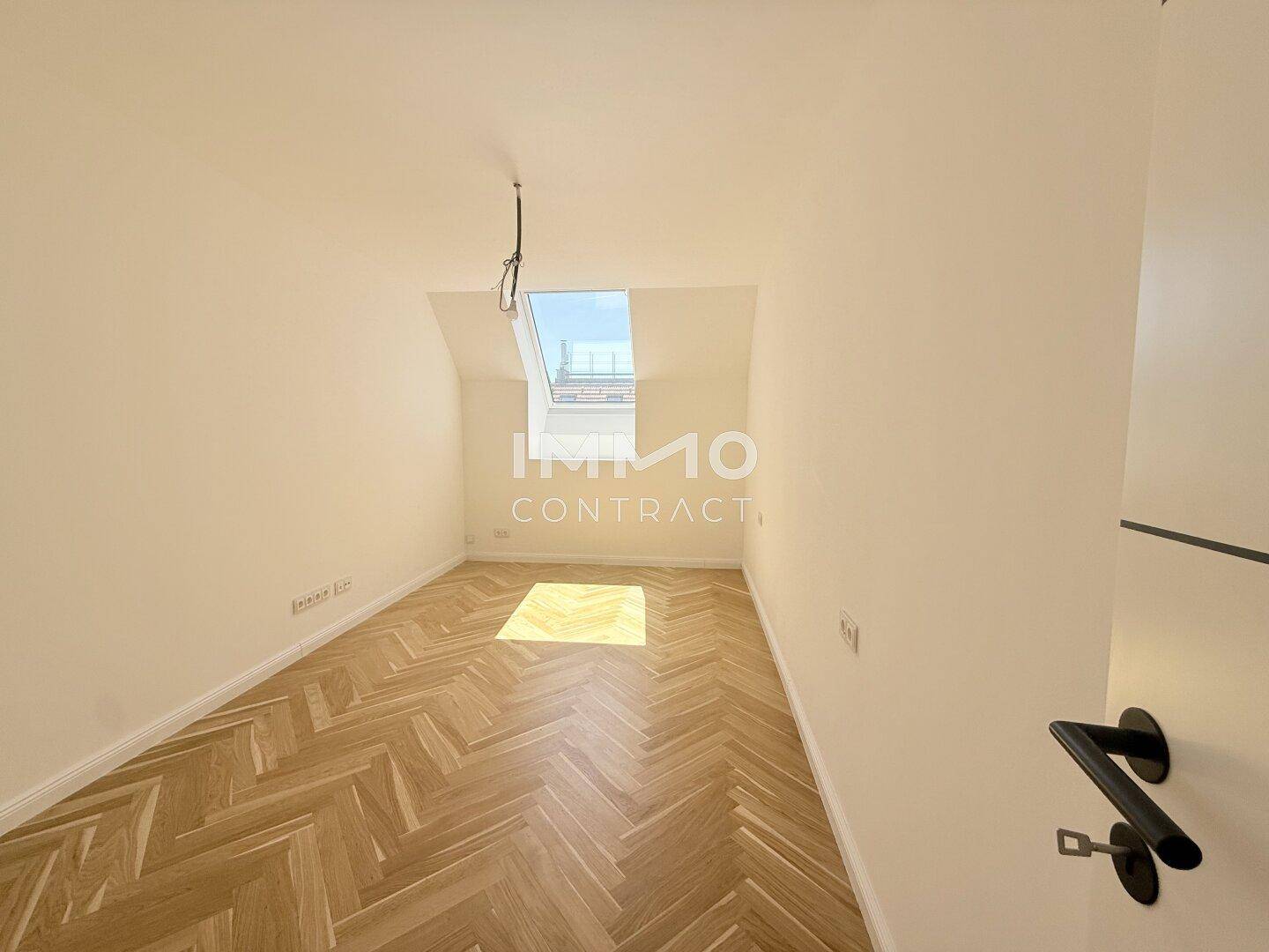 Helles Schlafzimmer mit Fischgrätparkett, Dachschräge und einem Dachfenster für natürliches Licht.