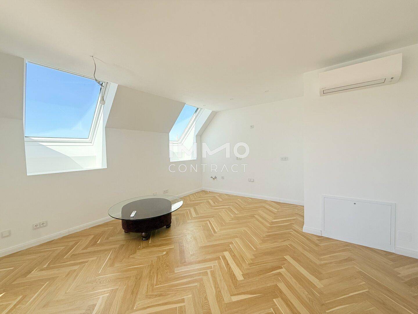 Heller Wohnbereich mit Fischgrätparkett, Dachfenstern und Klimaanlage an der Wand.