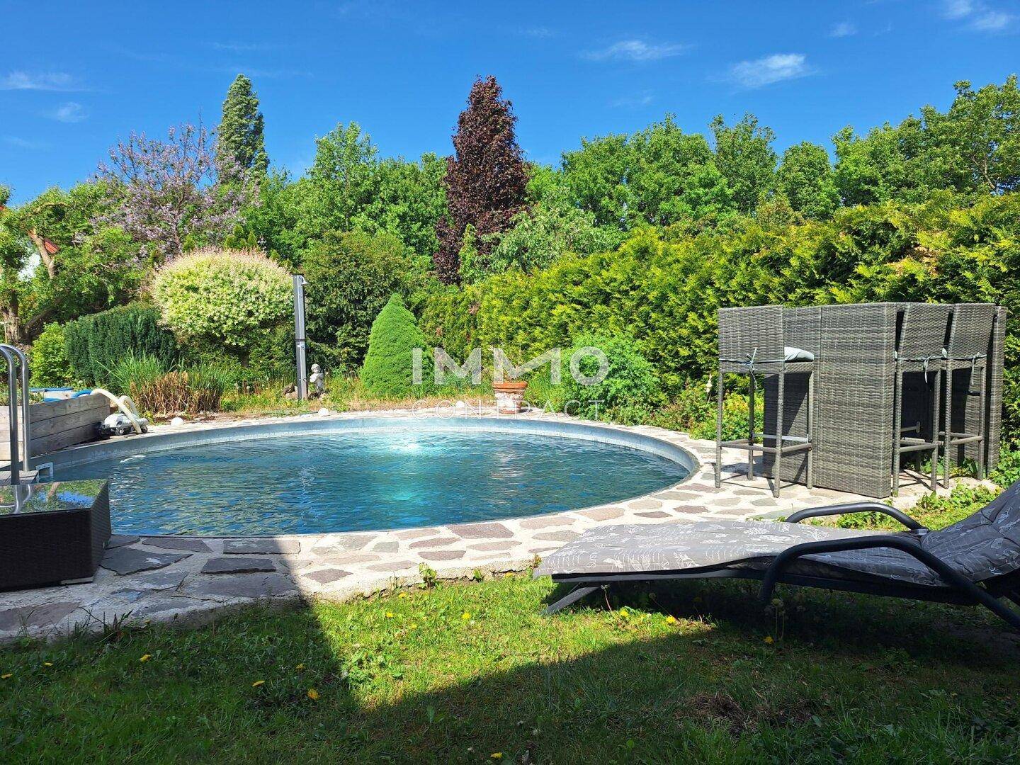 Sonnige Gartenoase mit rundem Pool, Liegestühlen und üppiger Bepflanzung.