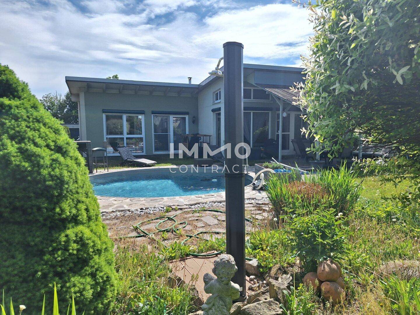 Blick auf das moderne Haus mit Pool und gepflegtem Garten unter strahlendem Himmel.