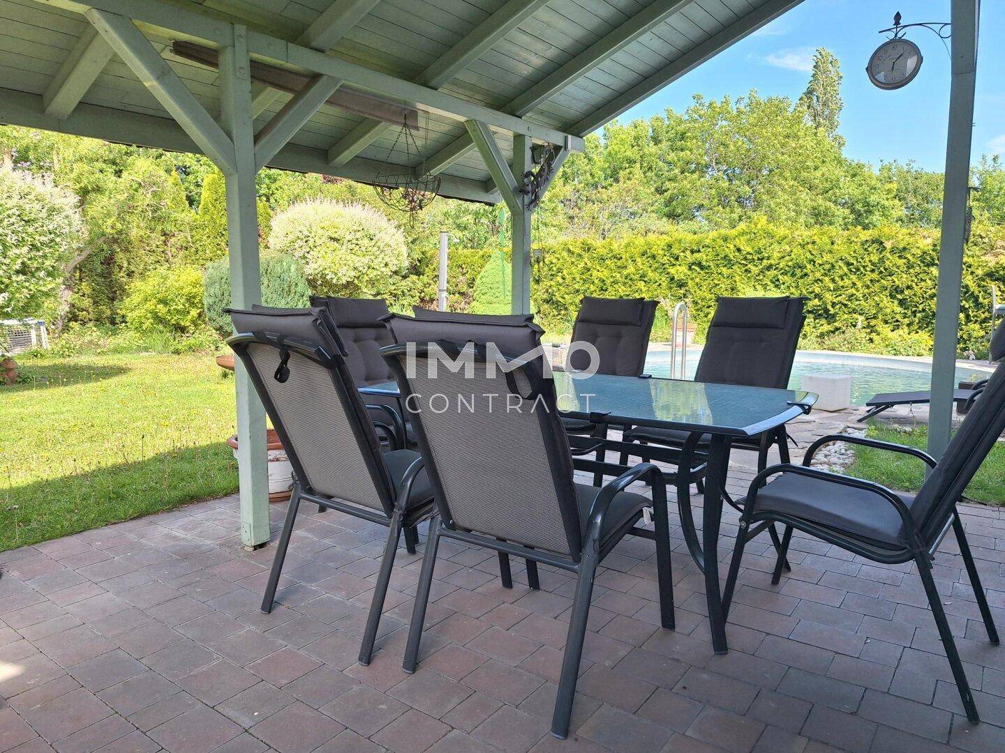 Gemütliche überdachte Terrasse mit großem Esstisch und Blick auf den Garten.