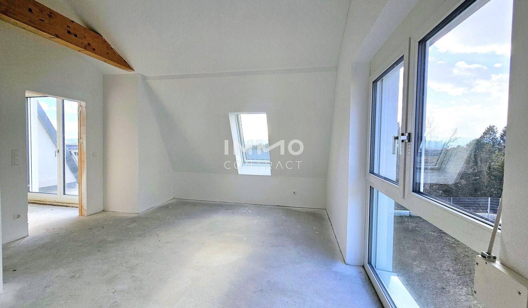 Heller Dachbodenraum mit sichtbaren Holzbalken, Dachschrägen und großen Fenstern mit Ausblick.
