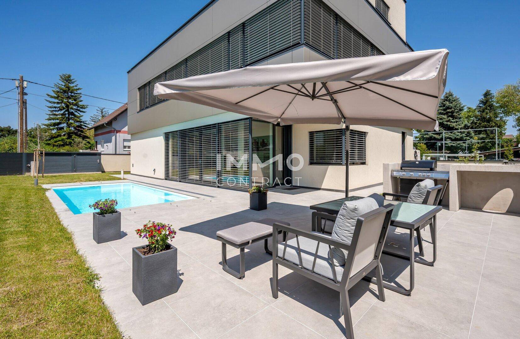 Außenbereich mit Swimmingpool, gepflasterter Terrasse und Rasenfläche, umgeben von grüner Natur.