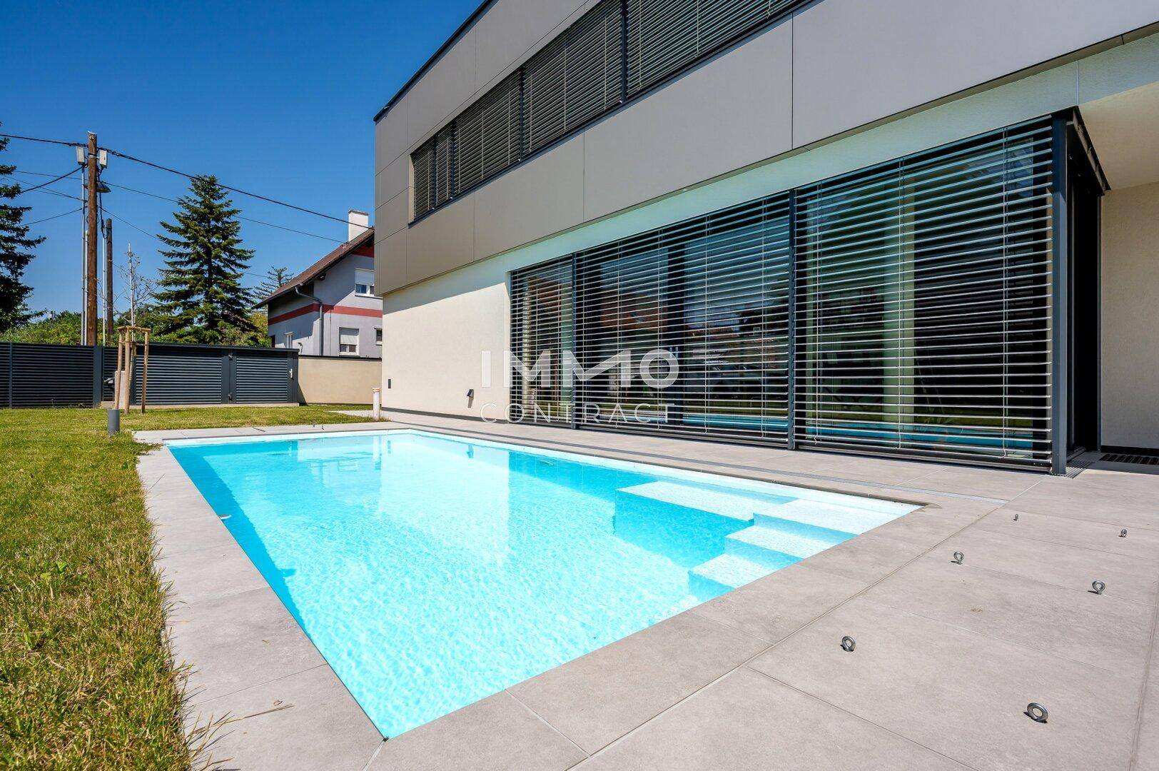 Moderner Swimmingpool mit einfacher Einstiegstreppe, umgeben von einer gepflegten Rasenfläche.