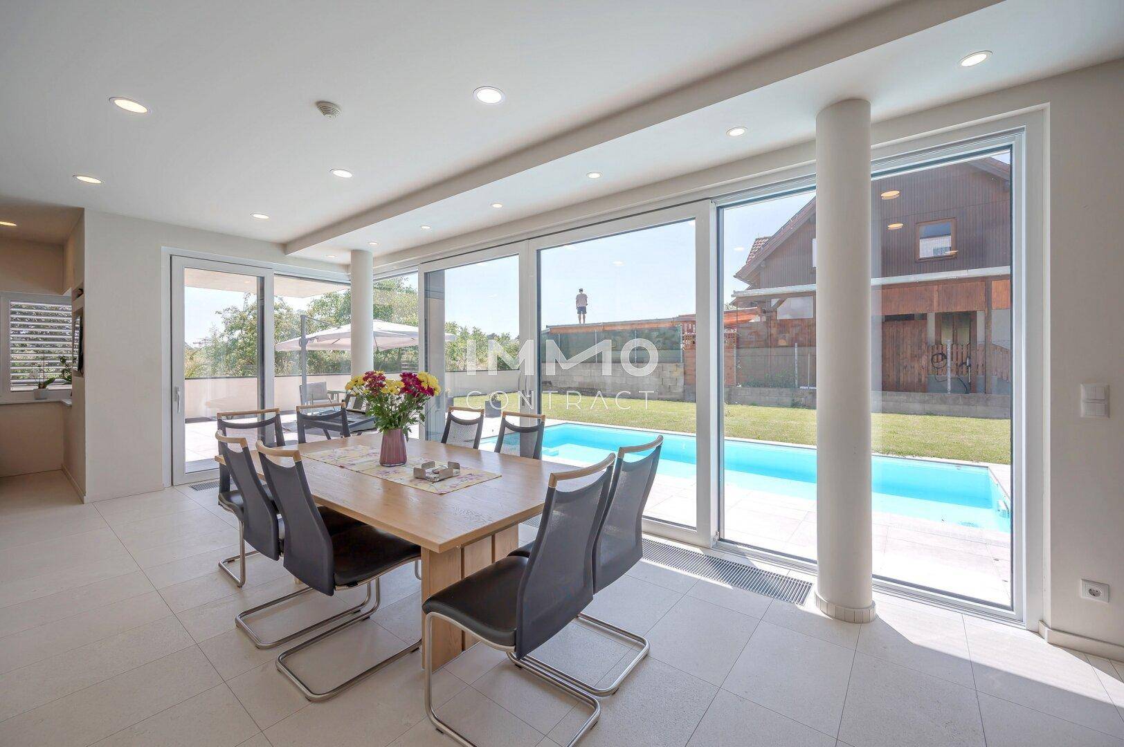 Essbereich mit Blick auf den Swimmingpool und den Garten durch große, lichtdurchflutete Fenster.