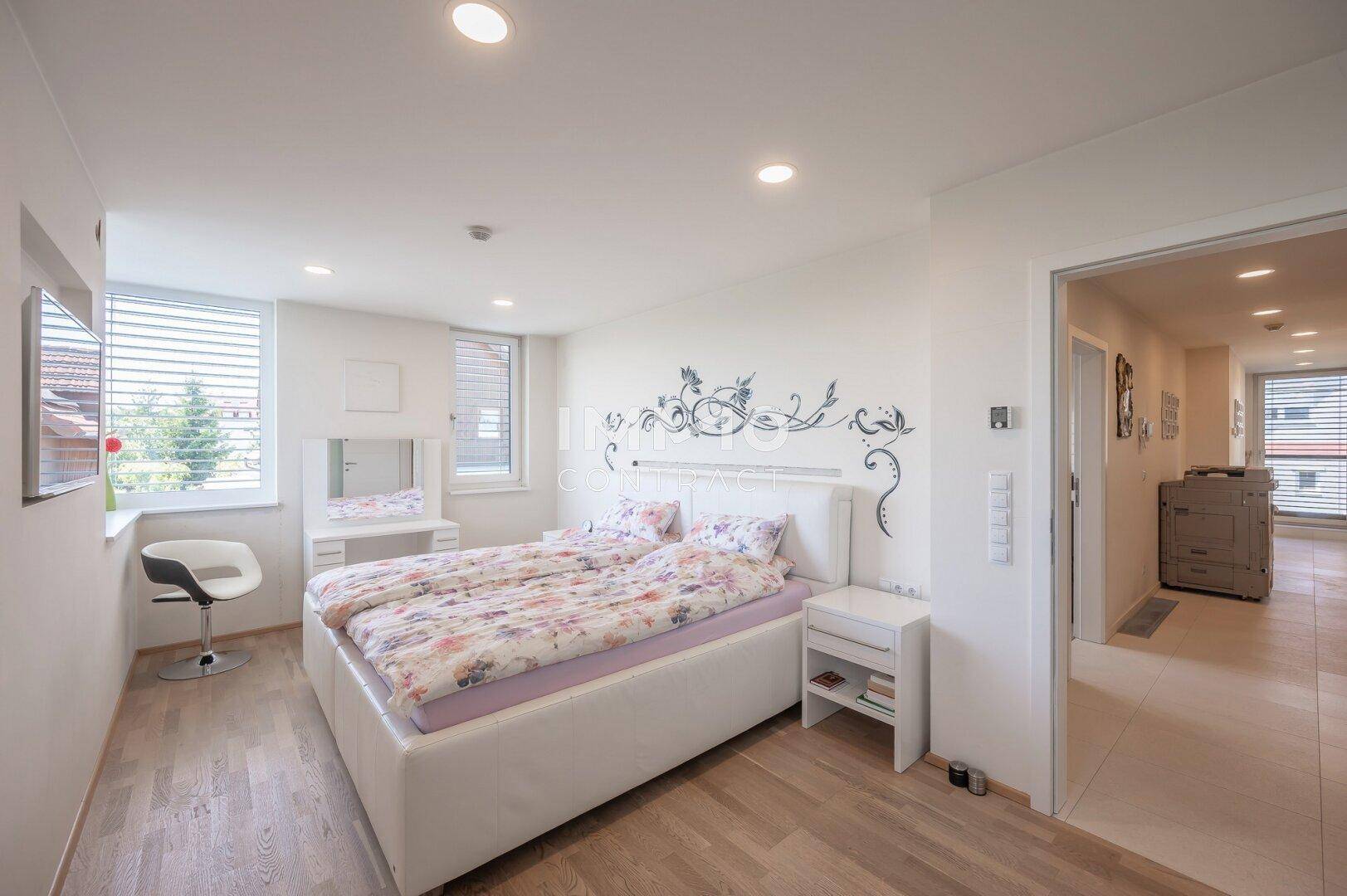 Helles Schlafzimmer mit Holzboden, großem Bett und zwei Fenstern für viel Tageslicht.