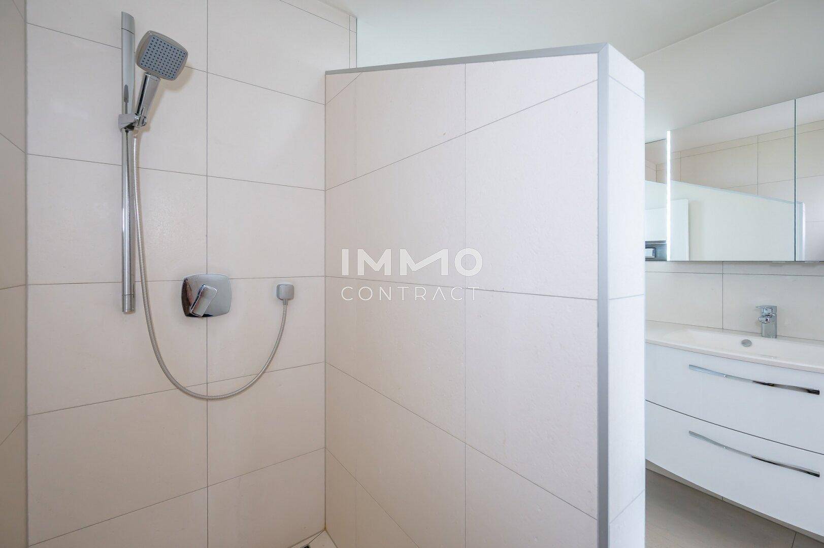 Moderne Dusche mit Handbrause und gefliesten Wänden in einem hellen Badezimmer.