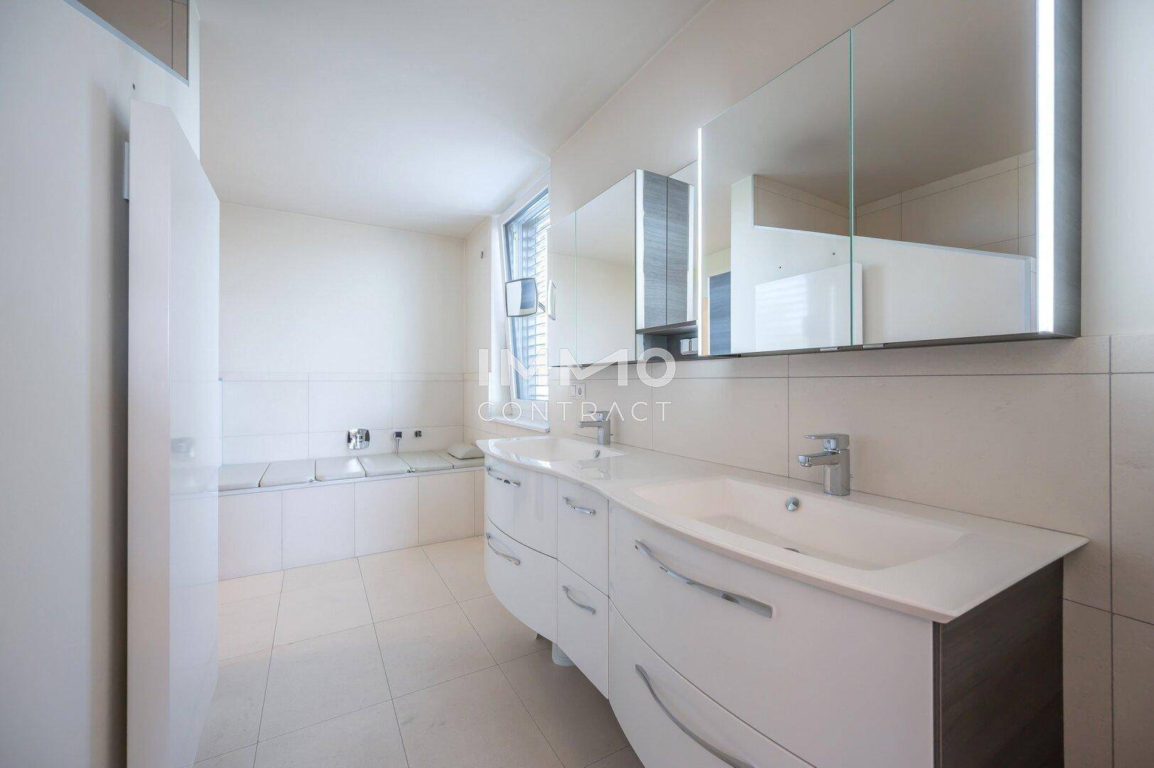 Geräumiges Badezimmer mit Doppelwaschbecken, großem Spiegel und integrierter Badewanne.