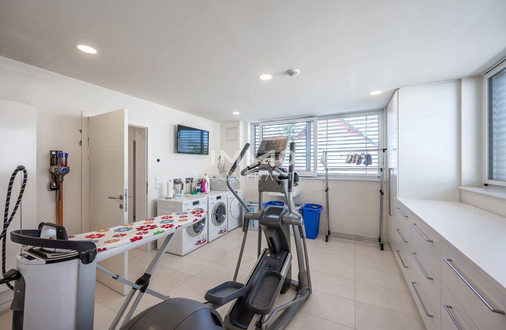 Geräumiger Hauswirtschaftsraum mit Waschmaschinen, Bügelbrett und Fitnessgeräten.