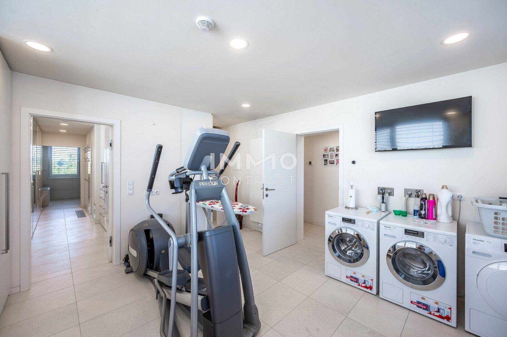 Heller Hauswirtschaftsraum mit Waschmaschinen und einem Crosstrainer für sportliche Aktivitäten.