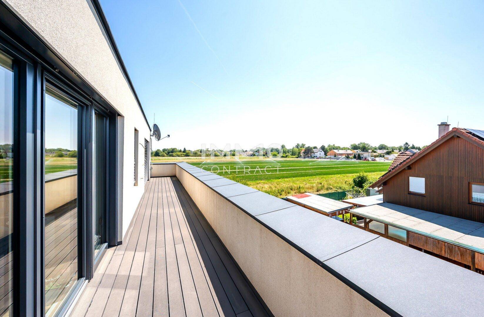 Langer Balkon mit Holzdielen und weitem Blick über grüne Felder und die Landschaft.