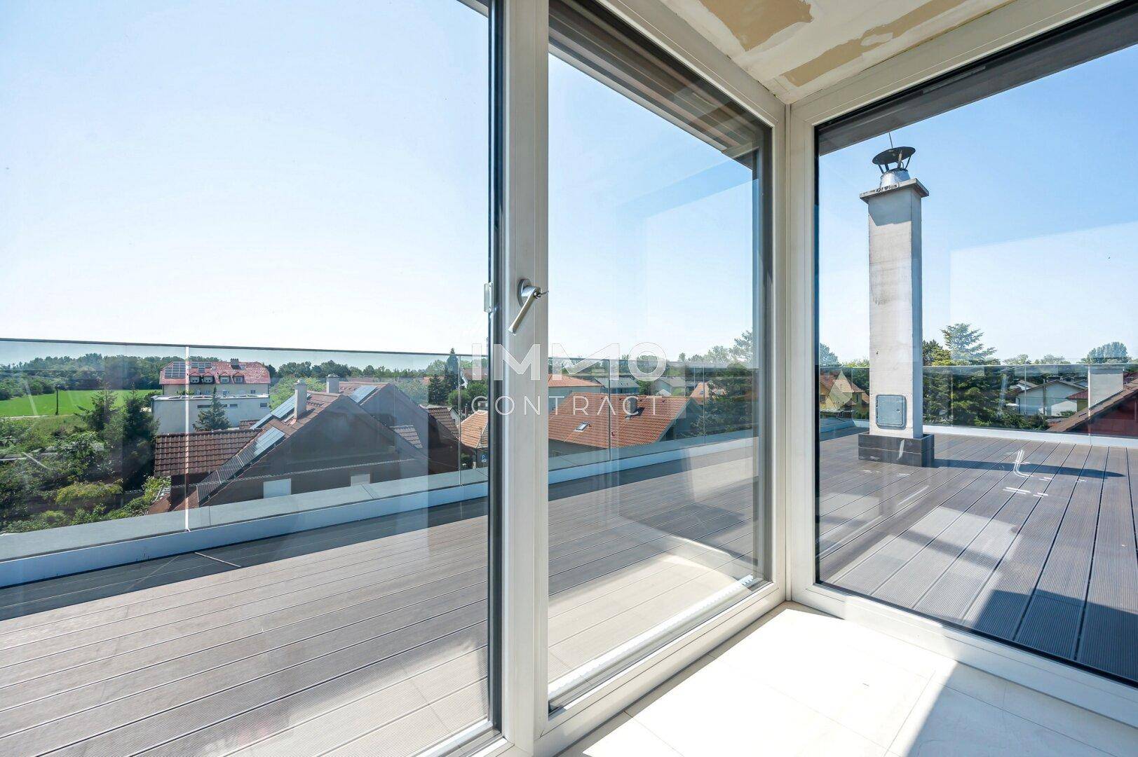 Große Glasfronten öffnen sich zu einer Dachterrasse mit weitem Blick über Dächer und Felder.