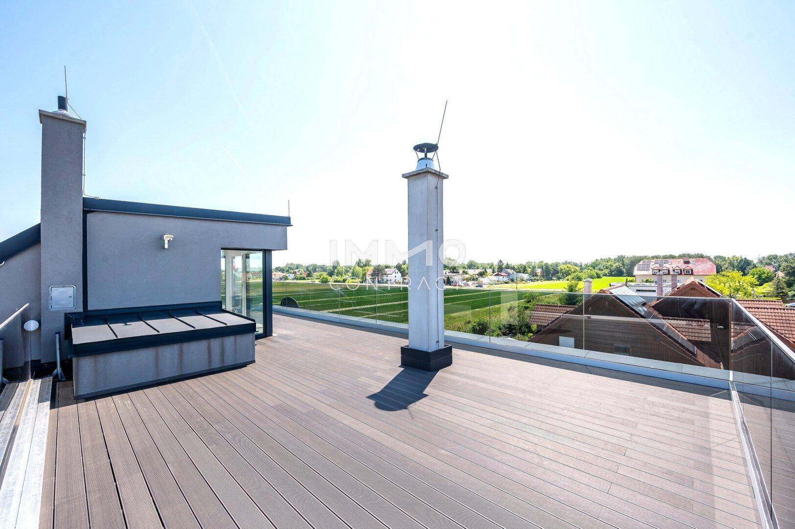 Weitläufige Dachterrasse mit Holzdielen und Kamin, bietet einen Panoramablick auf die Umgebung.